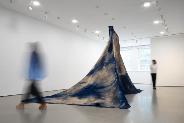 Visitors walk around a monumental sculpture made of blue and white dyed felt