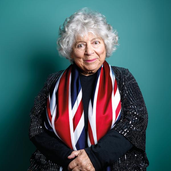 Miriam Margolyes smirks at the camera, sat with folded arms and a union flag draped around her sparkly cardigan.
