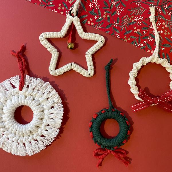A photograph of 4 macrame decorations laid against a red background, the decorations are in the shape of wreaths and stars in beige and green