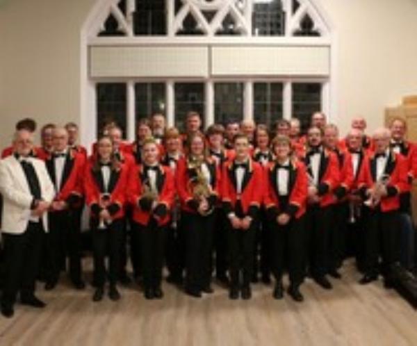 Very smart looking Brass Band dressed in red jackets with black lapels holding various brass instruments. They look like a very tidy bunch of people