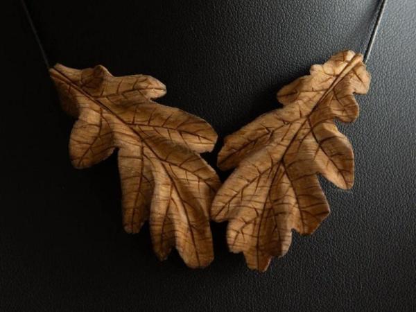 A necklace of two sculpted oak leaves made from wood.