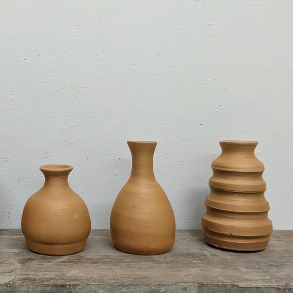 Three ceramic bottles sit on a wooden table, they are mid brown in colour and are organised in height order with the smallest being on the left.
