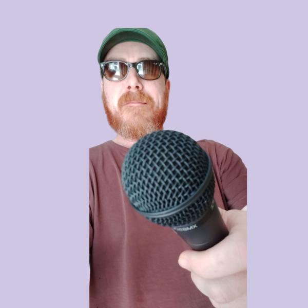 A photograph of a man wearing sunglasses holding out a microphone, the man is framed against a purple background