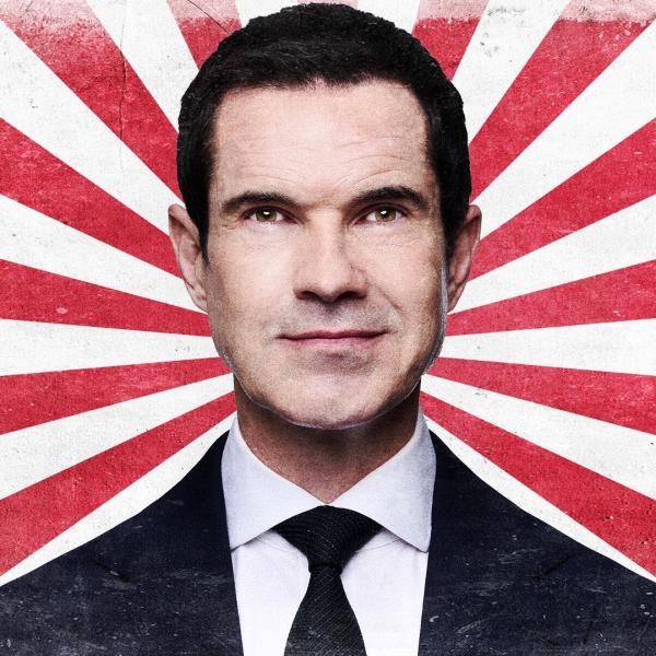 Jimmy Carr smirks in a black suit and tie, in front of a textured stripy red and white background.