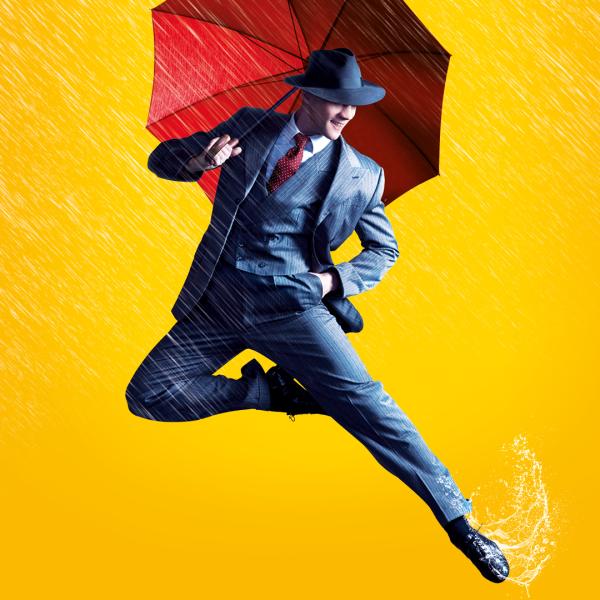 A man in a blue suit leaps into the air, holding a red umbrella and surrounded by rain against a yellow backdrop. 