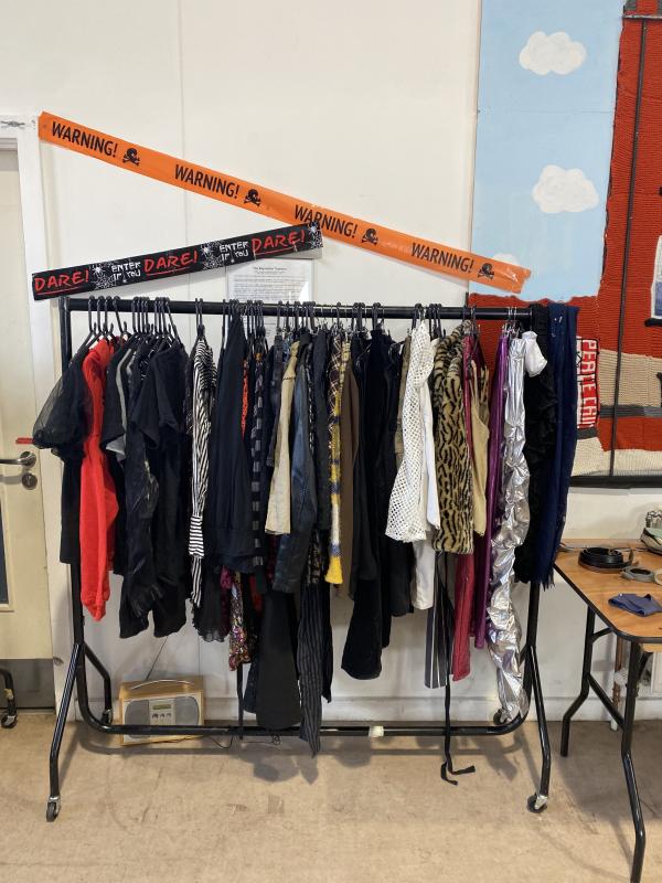 A rail of halloween costumes with novelty warning tape decorating the wall behind it.