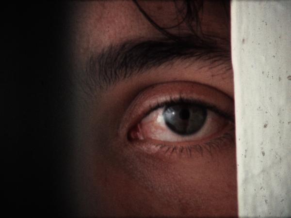 A young man's eye looks through a door frame