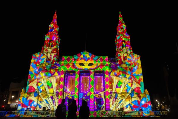 a large building at night lit up with a colourful projection and people watching