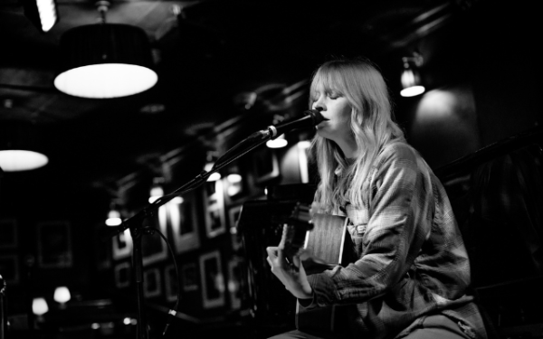 A woman singing on stage (Lucy Rose) with a guitar