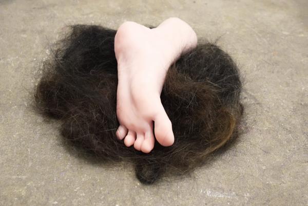A pale silicone foot sits on a pile of dark brown hair on a concrete floor