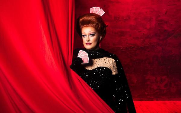 Kate Butch stands behind a red curtain, she holds a pack of cards.