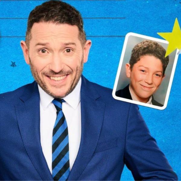 Jon Richardson grinning in a blue suit in front of a school textbook-style backdrop with doodles and a school photo of young Jon.