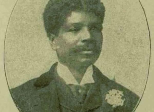 Historic portrait of a person in formal clothing with a moustache and a flower buttonhole, shown within an oval frame.