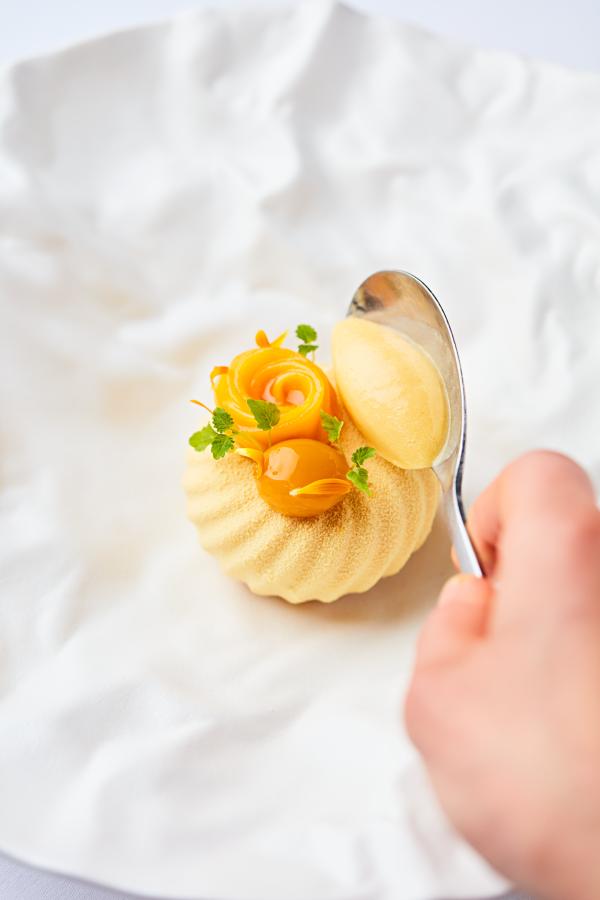 a hand holding a spoon placing a topping onto a pale pastry