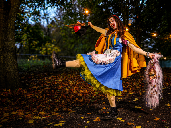 lady dressed as a dark version of Snow White, holding halloween props standing in a darkened woods
