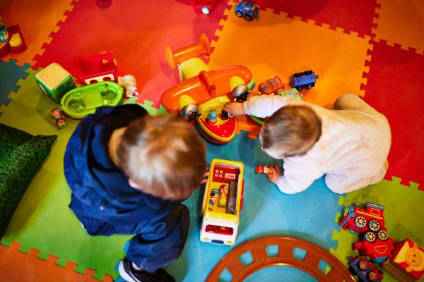 Toddlers playing with toys on a colourful play mat.