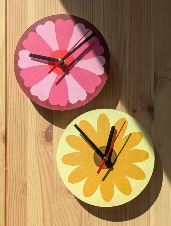 Two hand painted wall clocks with flower designs laid on a wooden surface