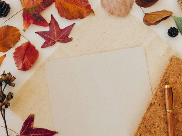 Image of autumnal leaves spread across a table next to a piece of paper and pen.