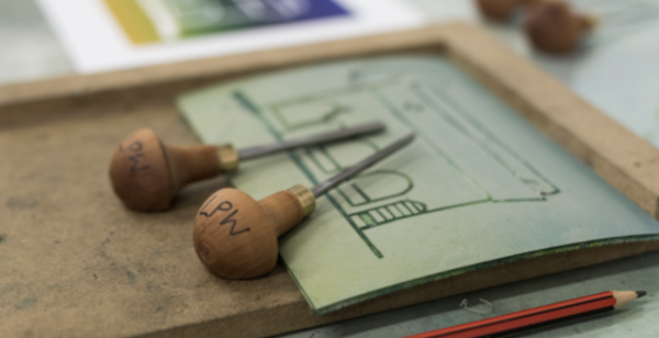 Lino cutting tools and a piece of lino with a design of a building carved into it