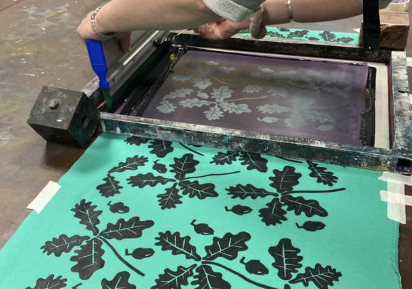 A repeated pattern of leaves being ecreen printed in black onto a green fabric