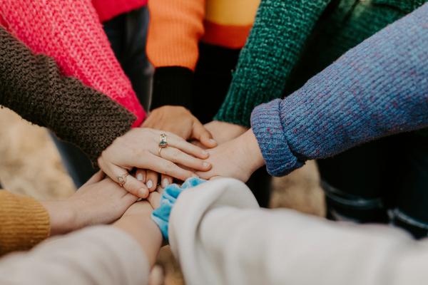 A group of people facing each other in a circle all put their hands together in the middle