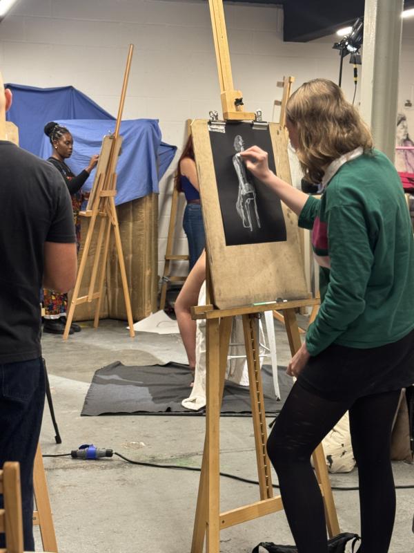 A life drawing class showing artists standing at easels drawing with white chalk on black paper