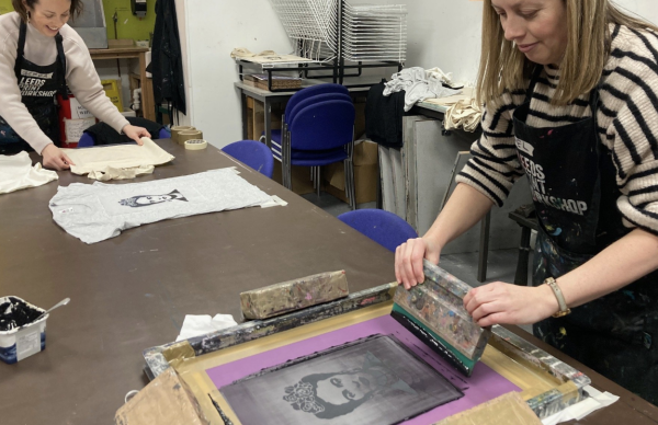 Two women screen printing images of Frida Kahlo onto t-shirts