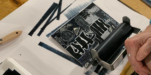 A person's hands rolling navy ink onto an abstract collagraph plate during a previous workshop.