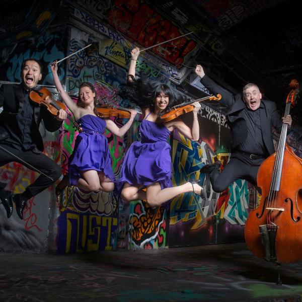 The quartet of Graffiti Classics jump up in the air with comic, open mouth expressions, each holding their instruments in a graffiti-covered tunnel.