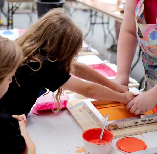 A child creates a screenprint with orange paint