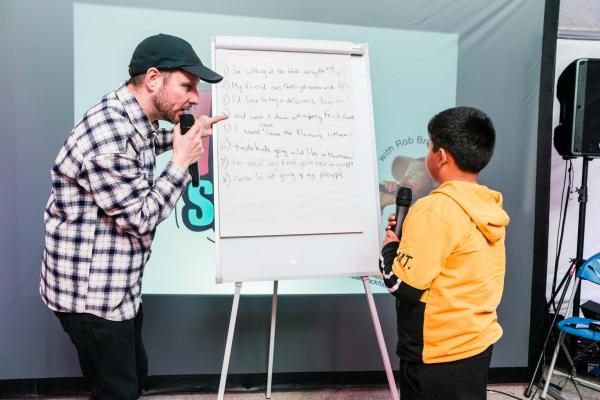 A rapper teaching a younger rapper using a flipchart