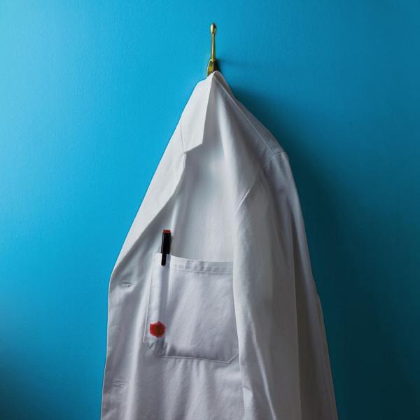 Against a blue backdrop, a white lab coat hangs on a clothes hook.