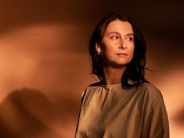 A woman with long dark hair wearing a gold-coloured top.