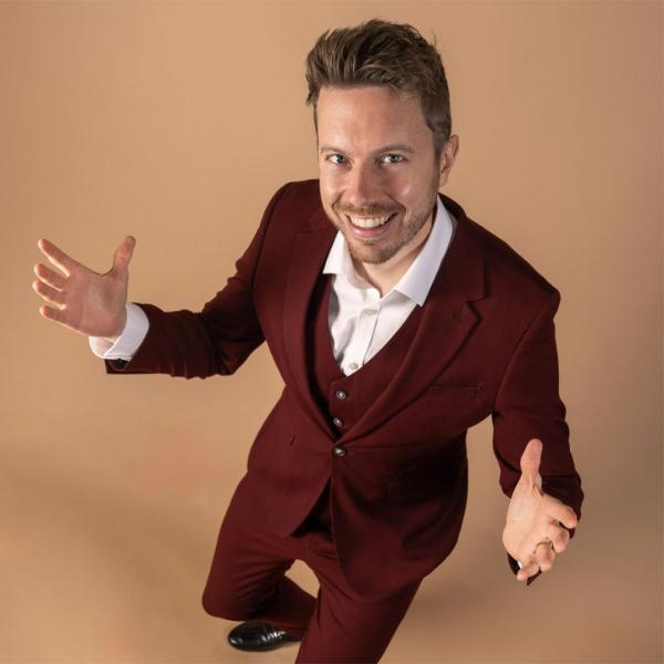 James B Partridge smiles in a maroon suit, with arms open.