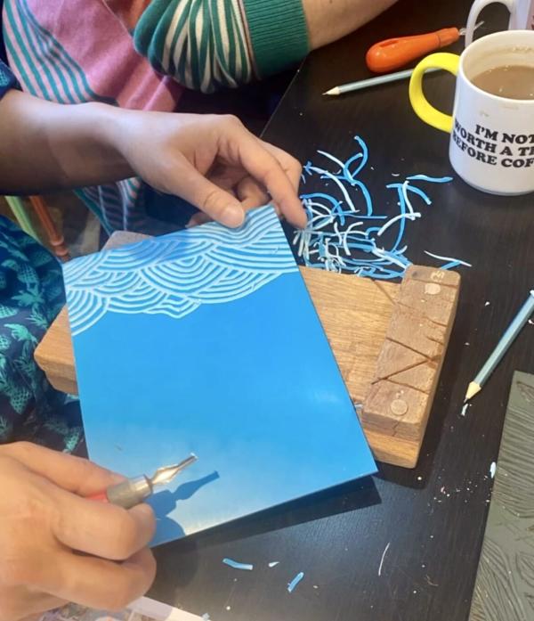 A sheet of bright blue lino being carved with curved lines.
