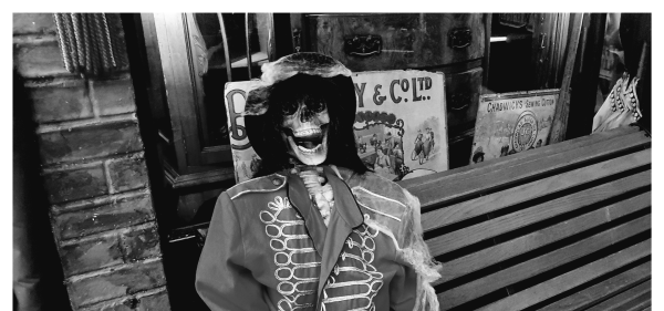 Black and white picture of a skeleton sitting on a bench in a Victorian Street display.