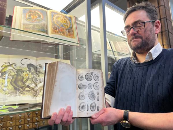 Image shows a man holding an open book showing fossil illustrations