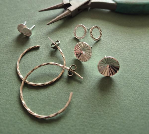 A pair of silver hoop earrings and three pairs of stud earrings laid on a green background with some pliers in the background