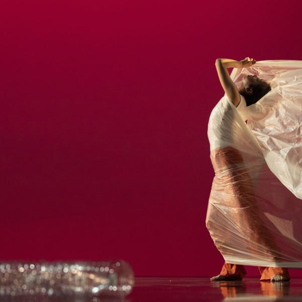 Dancer pulls plastic sheet across stage against a bright red background