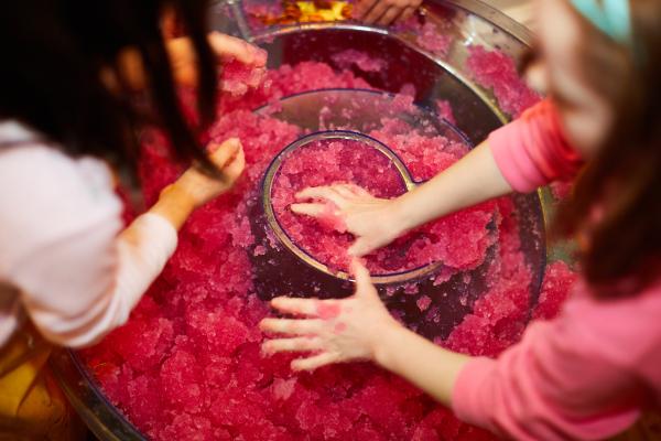 Two children taking part in a hands-on science experiment with a pink substance.