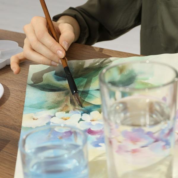 A watercolour painting of flowers, a hand holds a paintbrush over the painting 