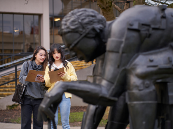 Two people holding clipboards and drawing a bronze sculpture of a man bent over in thought