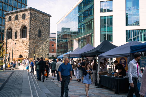 This picture is a group of market stalls in Wellington Place, with lots of shoppers wandering around.