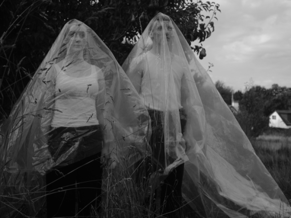 Two people stand with veils of plastic covering them 