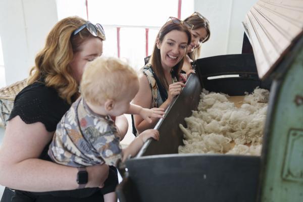 3 adults and a toddler looking into a industrial machine with wool in