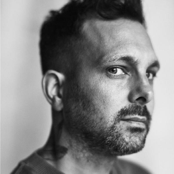 Black and white headshot of Dynamo looking sideways at the camera.