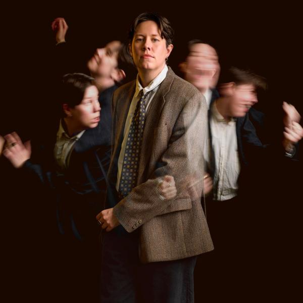 Chloe Petts stands in a tweed jacket, shirt and tie, surrounded by four blurred versions of herself in motion. 