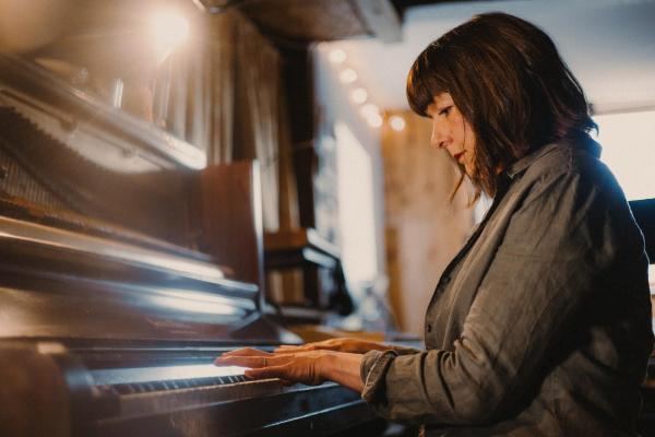 Emily sat at a wooden piano, focused whilst playing it