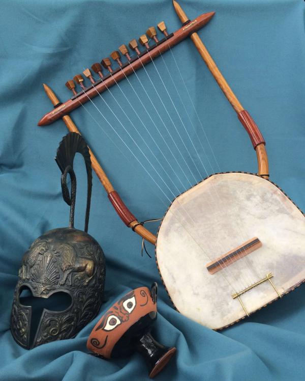 An ancient Greek Helmet lie beside a goblet decorated with eyes and an ancient stringed instrument