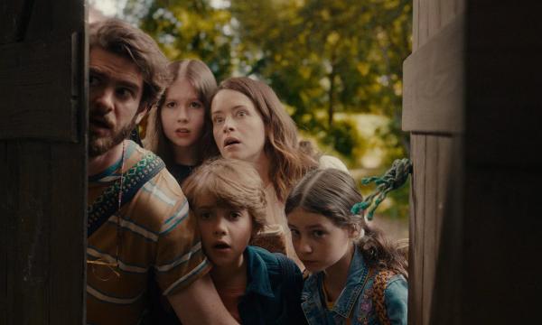 A family, a man, three children and a woman peer around a doorframe with shocked faces